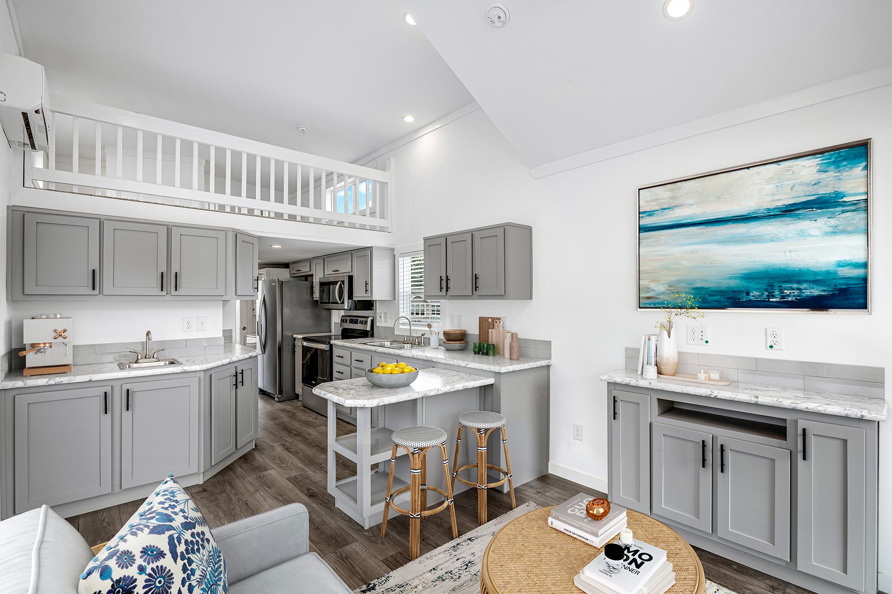 Modern kitchen-living area with gray cabinetry, stainless steel appliances, and a marble-topped island with stools. Bright, cozy, and inviting.