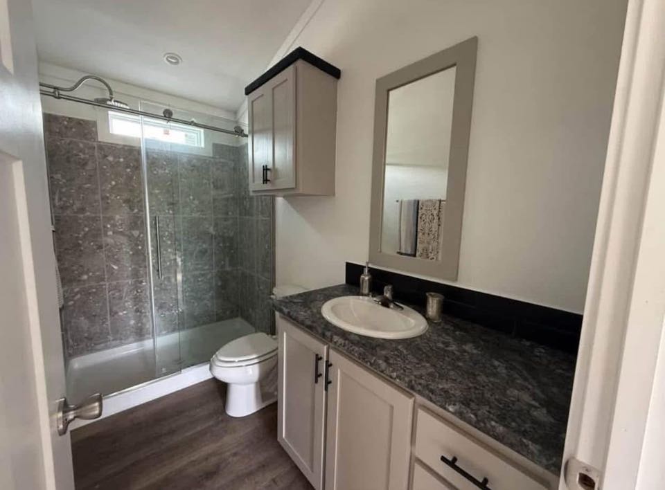 Small bathroom with a modern, sleek design. Features a glass-enclosed shower with stone tiles, a white toilet, and a gray vanity with a rectangular mirror.