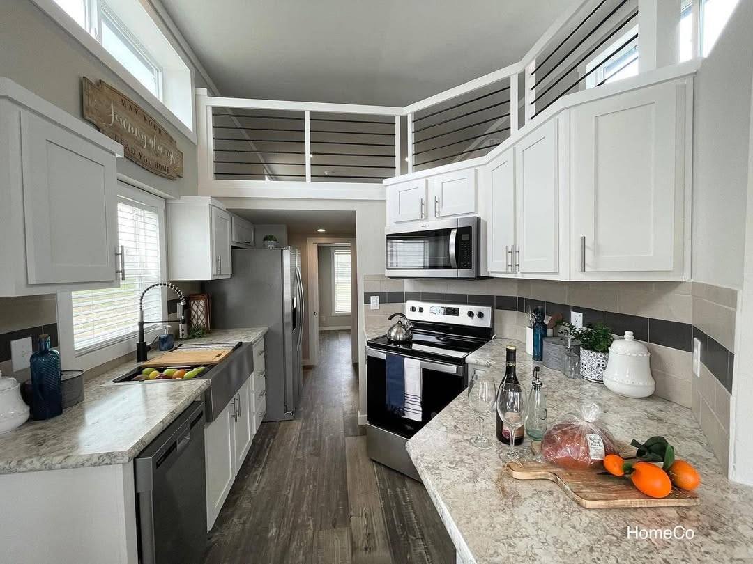 Modern kitchen with white cabinets, granite countertops, and stainless steel appliances. Bright light from windows creates an inviting atmosphere.