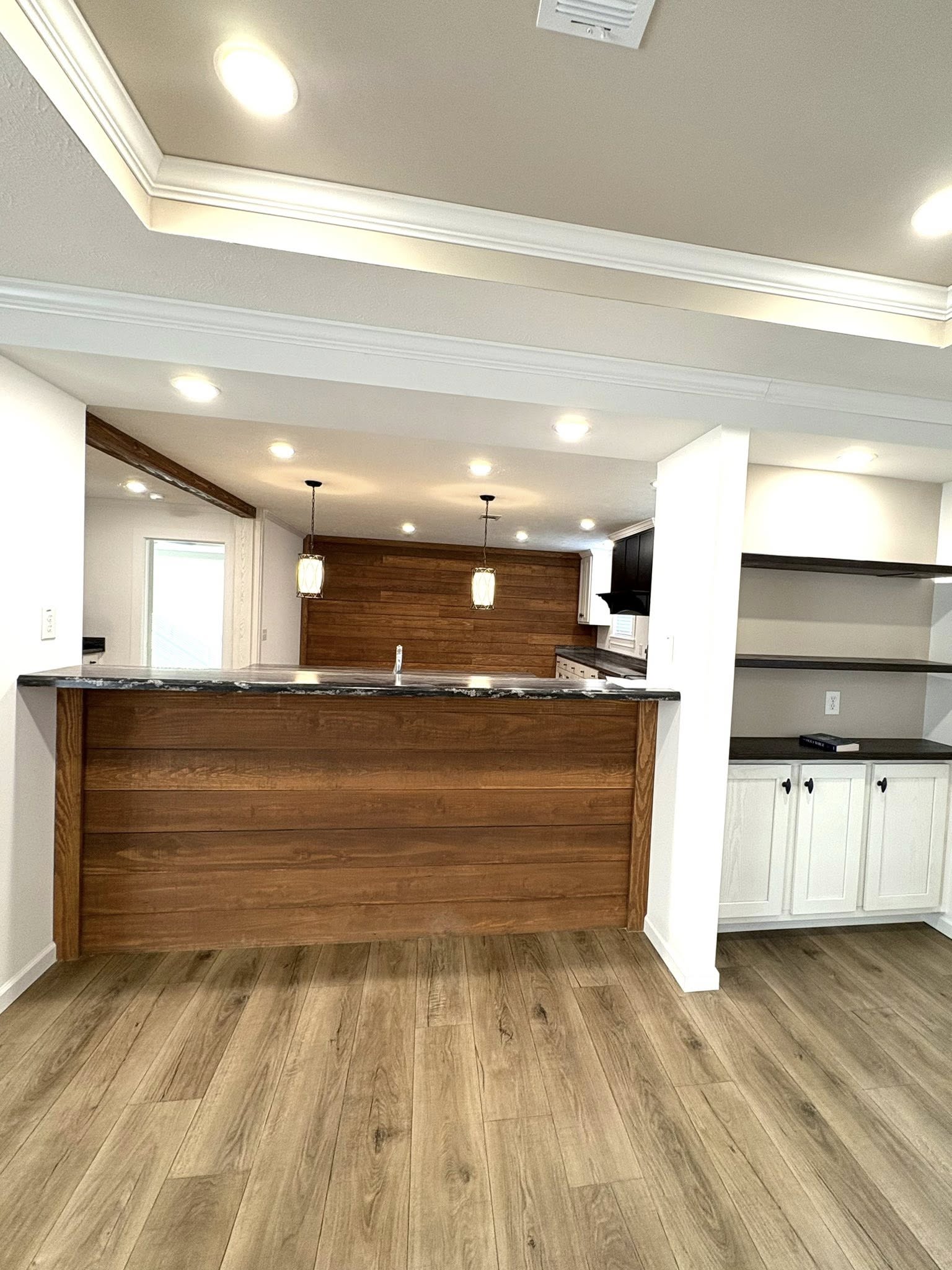 Modern kitchen with wood accents and white walls. Features a wooden island with granite top, pendant lights, open shelves, and recessed lighting. Cozy and inviting.
