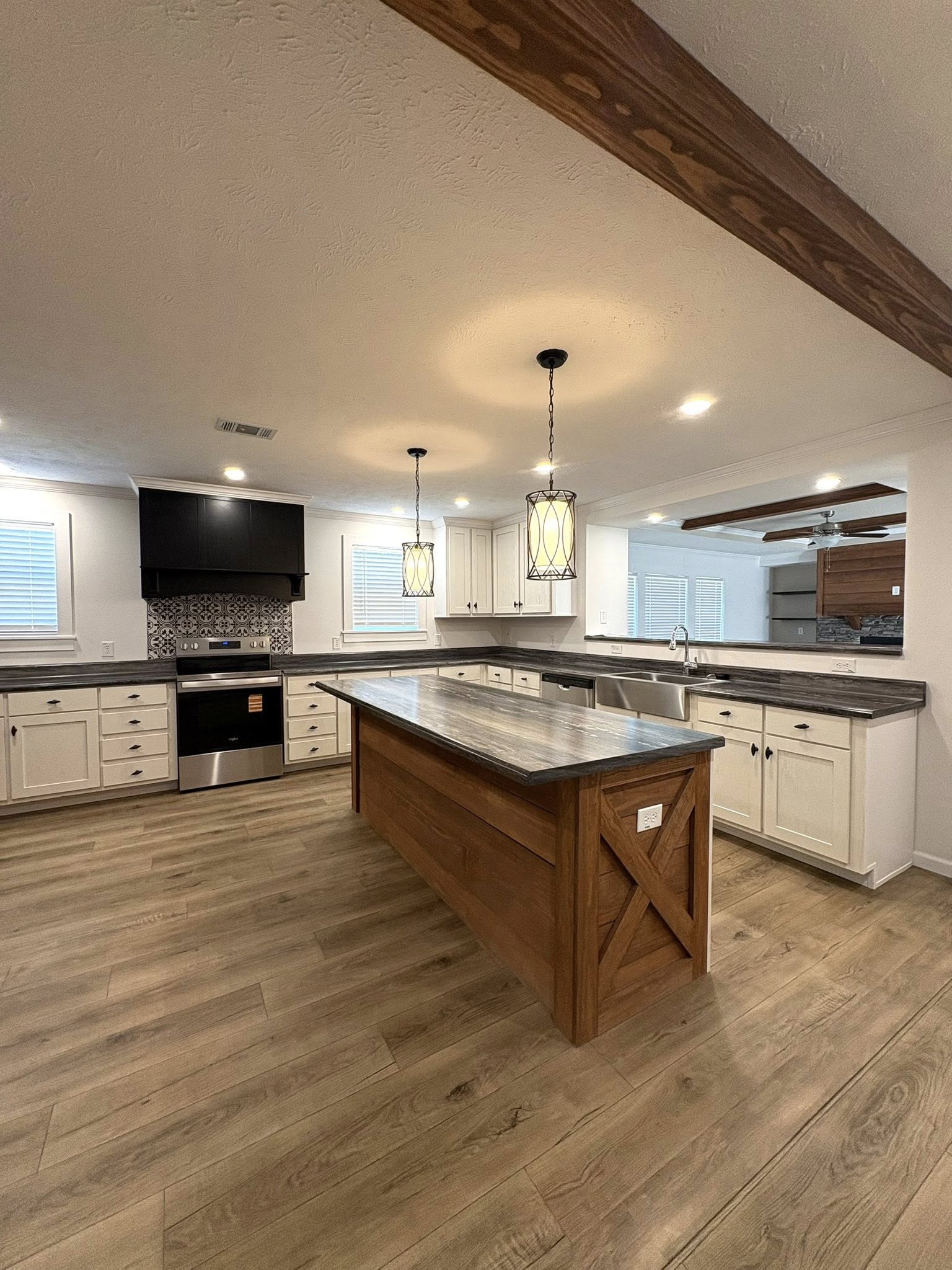 Spacious kitchen with a central wooden island, modern appliances, white cabinets, and pendant lights. Hardwood floor adds a warm, inviting feel.