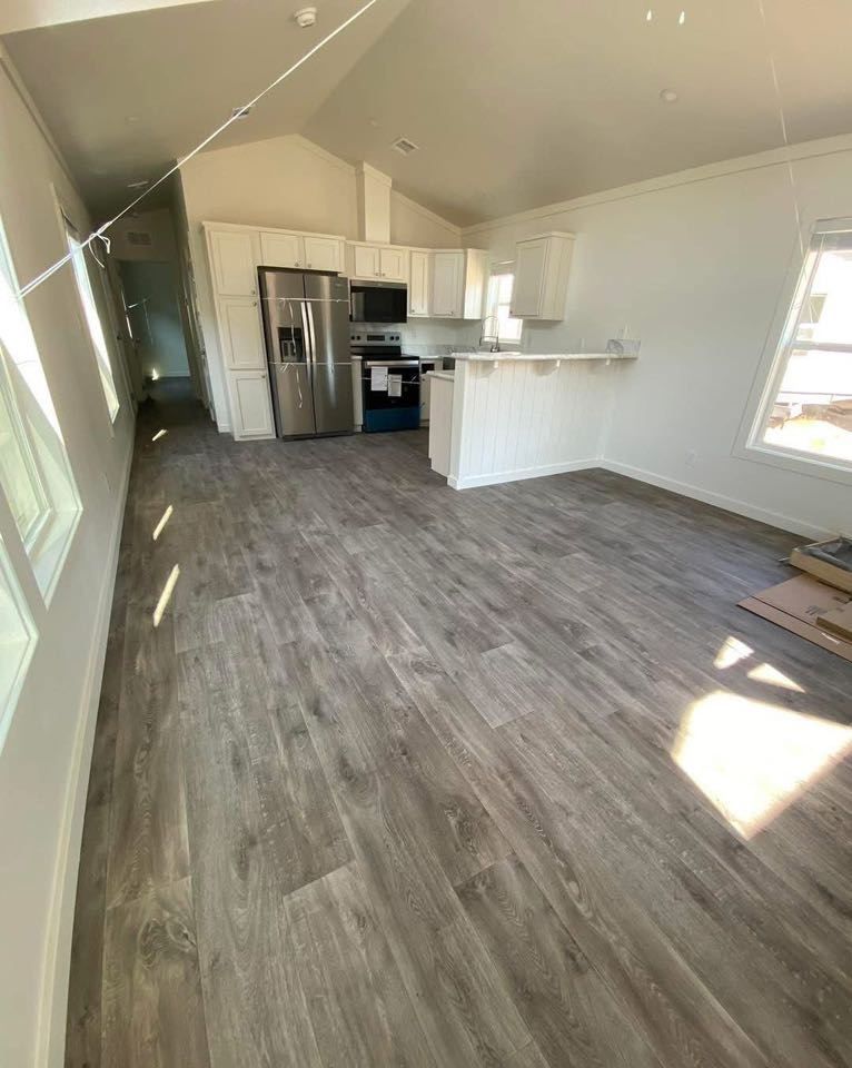 Spacious kitchen with light wood flooring, white cabinets, and stainless steel appliances. Sunlight streams through windows, creating a warm ambiance.