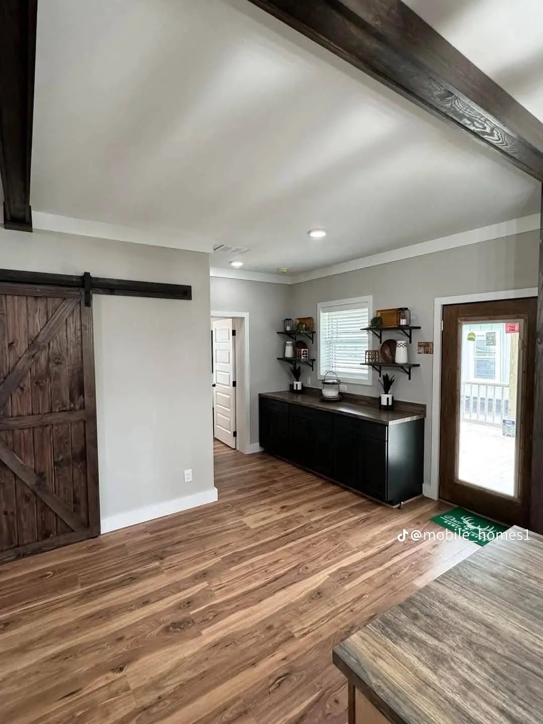 Modern kitchen with wooden floors, a rustic sliding barn door, dark cabinets, and open shelves; bright with natural light and cozy ambiance.