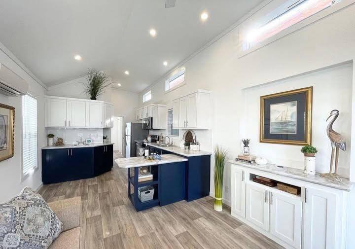 Modern kitchen with white and navy cabinets, marble countertops, and wood flooring. Art and decor, including a sailboat painting and a heron sculpture, add elegance.