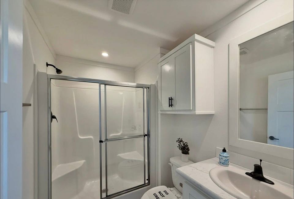 A clean, modern bathroom with a glass-enclosed shower, white vanity, and marble countertop. Subtle lighting and minimal decor create a calm atmosphere.