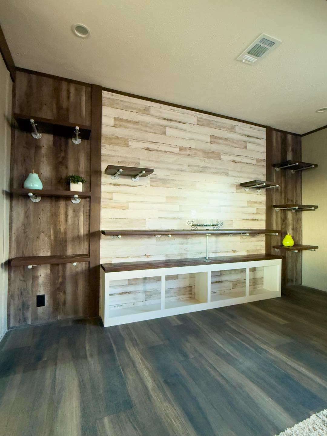 Modern room interior with a wood panel accent wall and dark wood flooring. Floating shelves display decorative items in a warm, minimalistic setting.