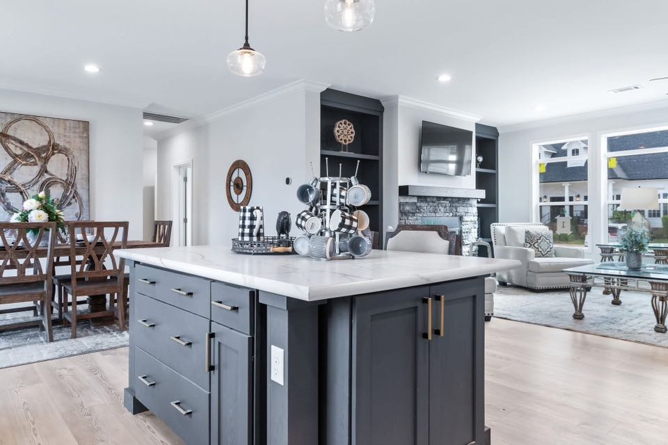 Modern open-plan kitchen and living area with dark cabinets, white marble island, and light wood floors. Dining table, cozy seating, and bright windows.