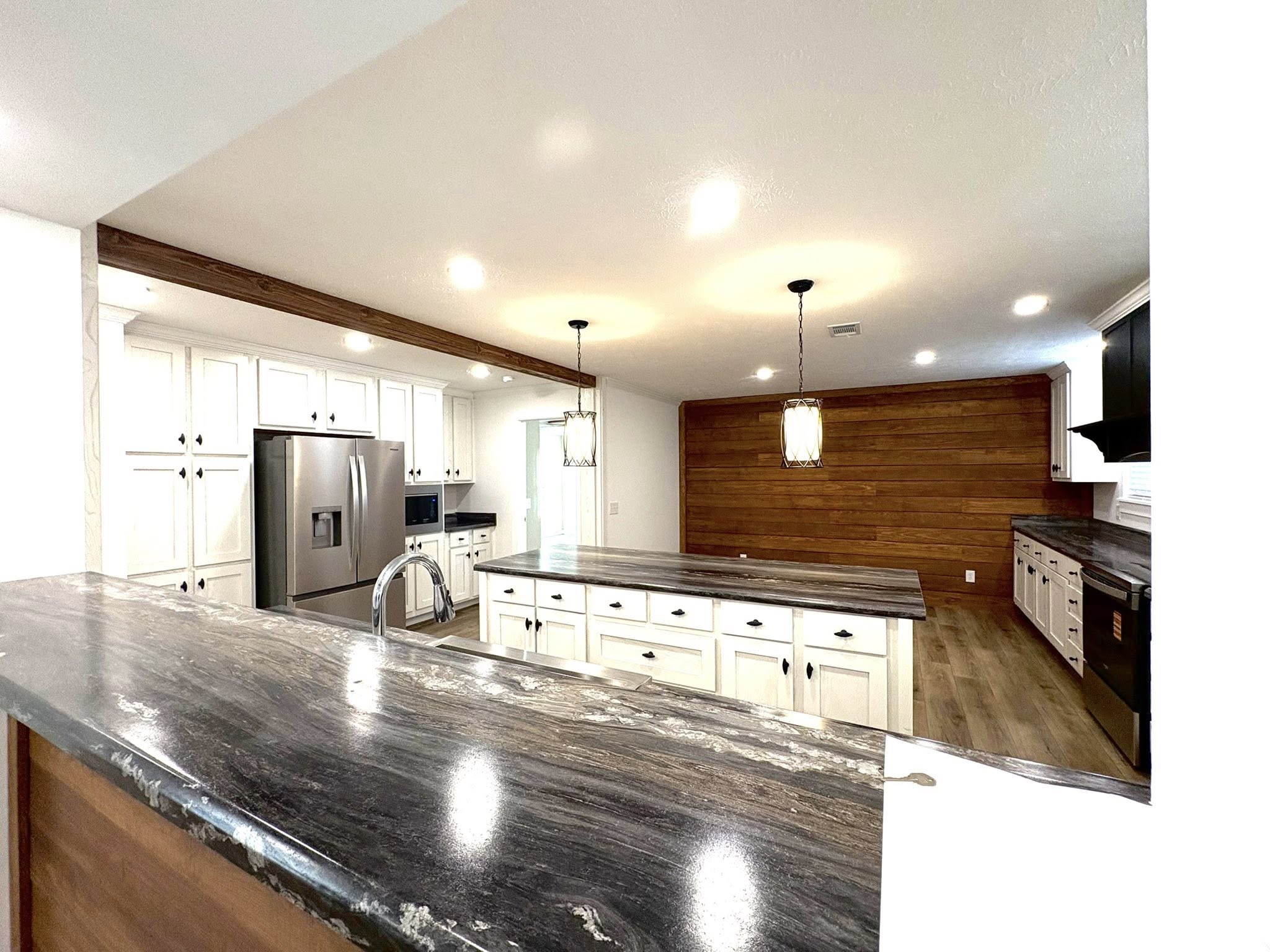Spacious modern kitchen with white cabinets, stainless steel appliances, and a large island with dark countertops. Wood-paneled wall adds warmth.