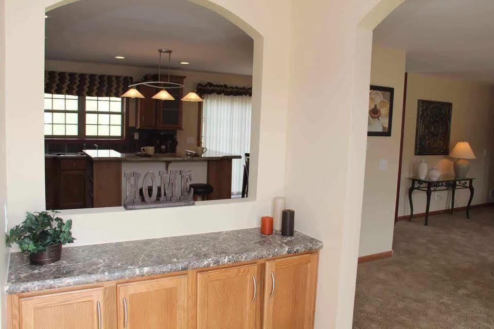 Cozy living space with a kitchen view through an arched opening. A marble countertop holds candles and a plant, creating a warm, inviting atmosphere.