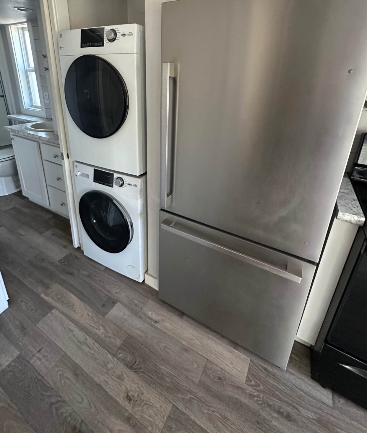 Stacked washer and dryer next to a stainless steel fridge in a compact kitchen with wooden floors. Bright, modern, and efficient space.