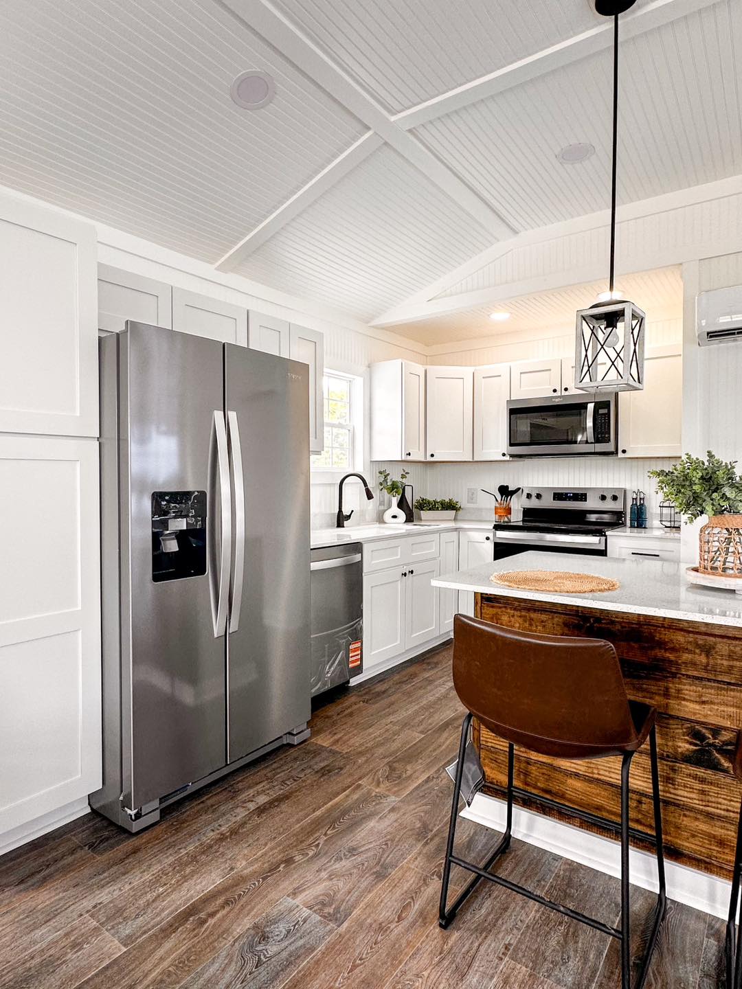 Modern kitchen with white cabinets, stainless steel appliances, a large fridge, and a wooden island. Brown chair and pendant light add warmth.