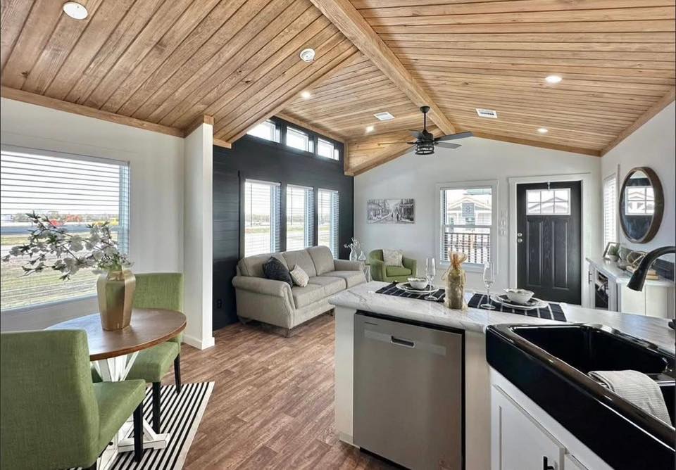 Cozy open-plan living room and kitchen with a wooden ceiling, modern furniture, and bright light from large windows. Neutral tones and natural textures.
