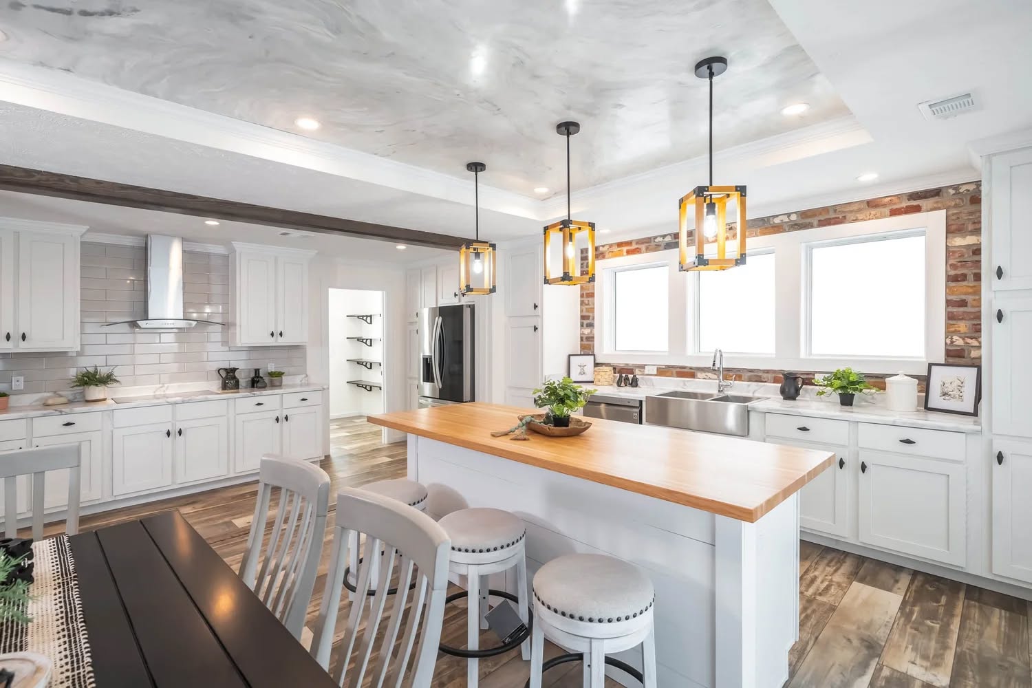 Bright kitchen with a wooden island, pendant lights, and white cabinets. Features modern decor, stainless steel appliances, and a cozy ambiance.