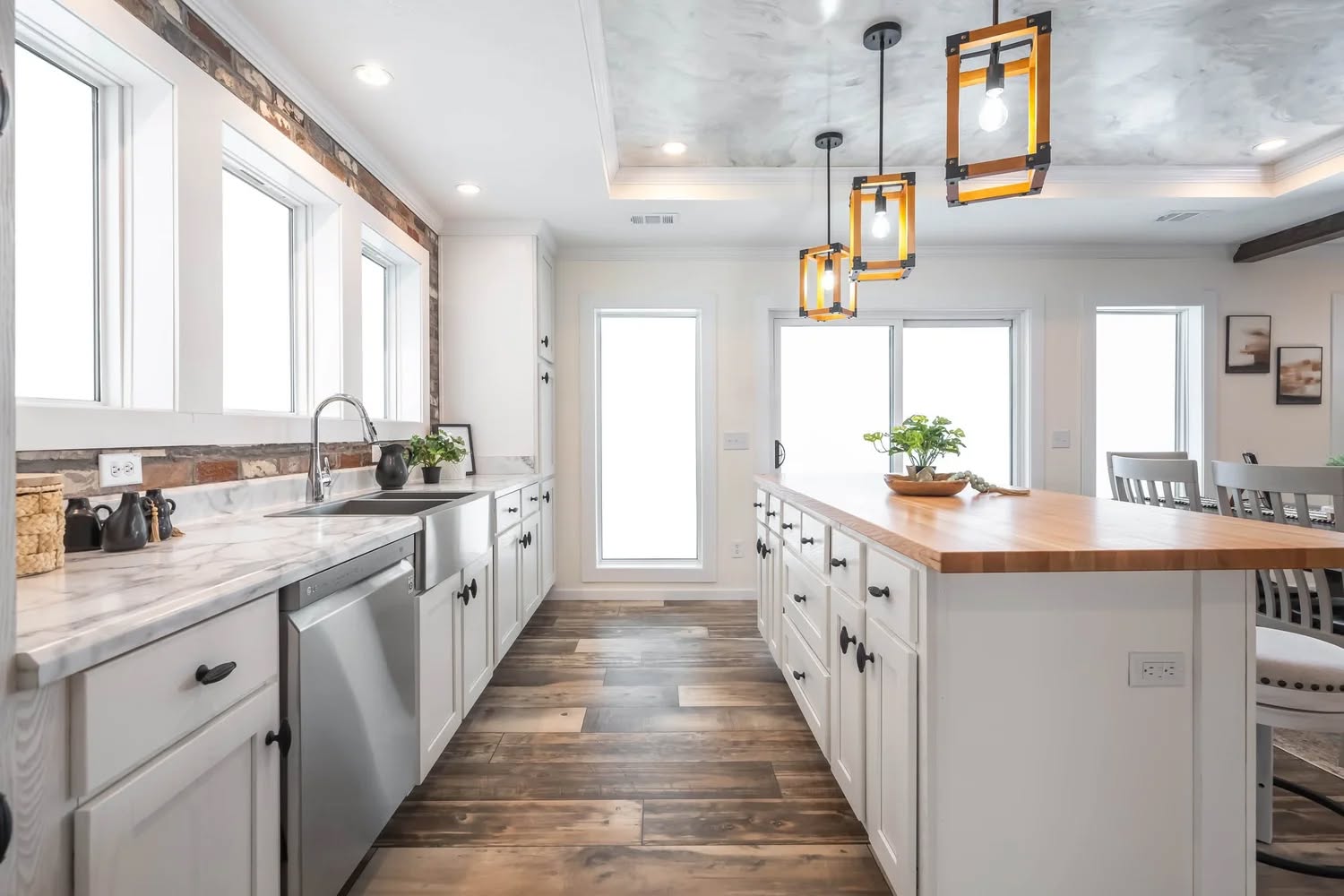 Bright, modern kitchen with white cabinets, marble countertops, and a wood island. Rustic lighting fixtures hang from the ceiling. Cozy and inviting.