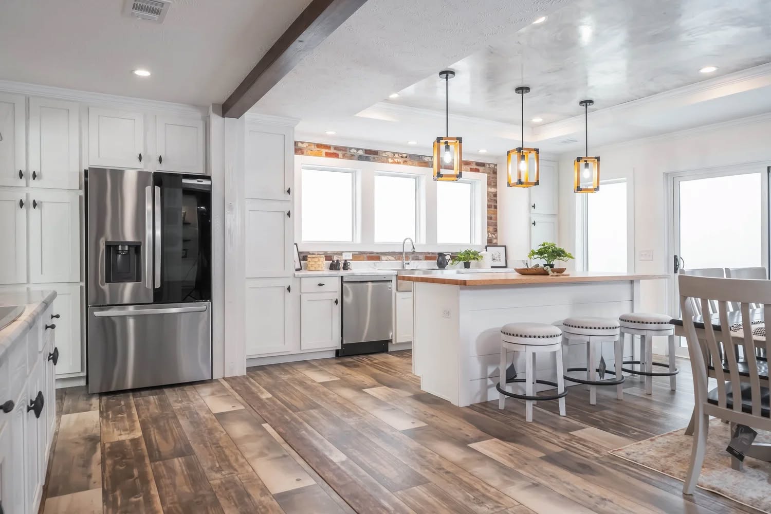 Bright, modern kitchen with white cabinetry, stainless steel appliances, and a wooden floor. Three pendant lights hang over a bar with stools, conveying a cozy, inviting atmosphere.