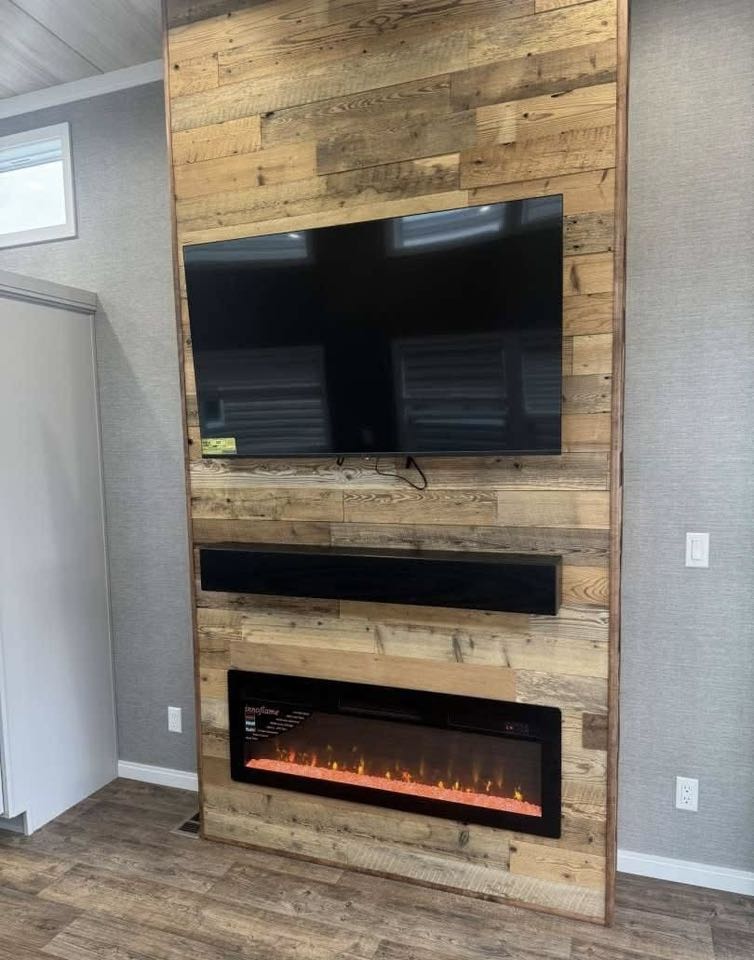 A modern living room wall features a mounted flat-screen TV, a sleek black soundbar, and an electric fireplace with glowing orange flames, set against rustic wooden panels.