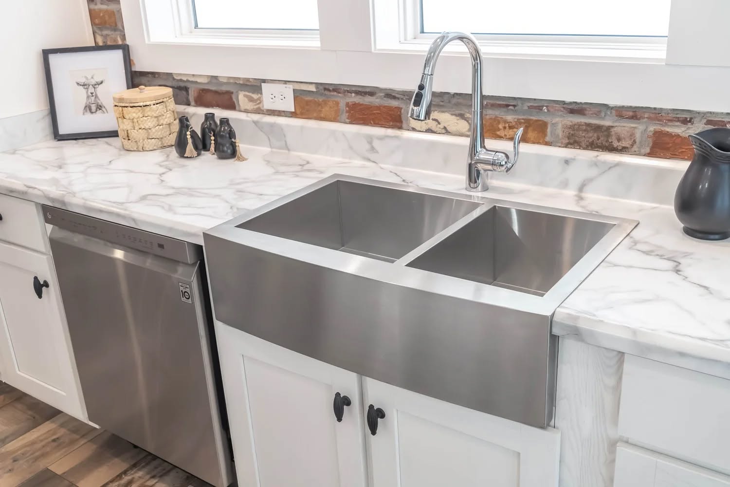 Modern kitchen with a stainless steel farmhouse sink and dual basins. Marble counters, brick backsplash, and black accents create a sleek, cozy feel.