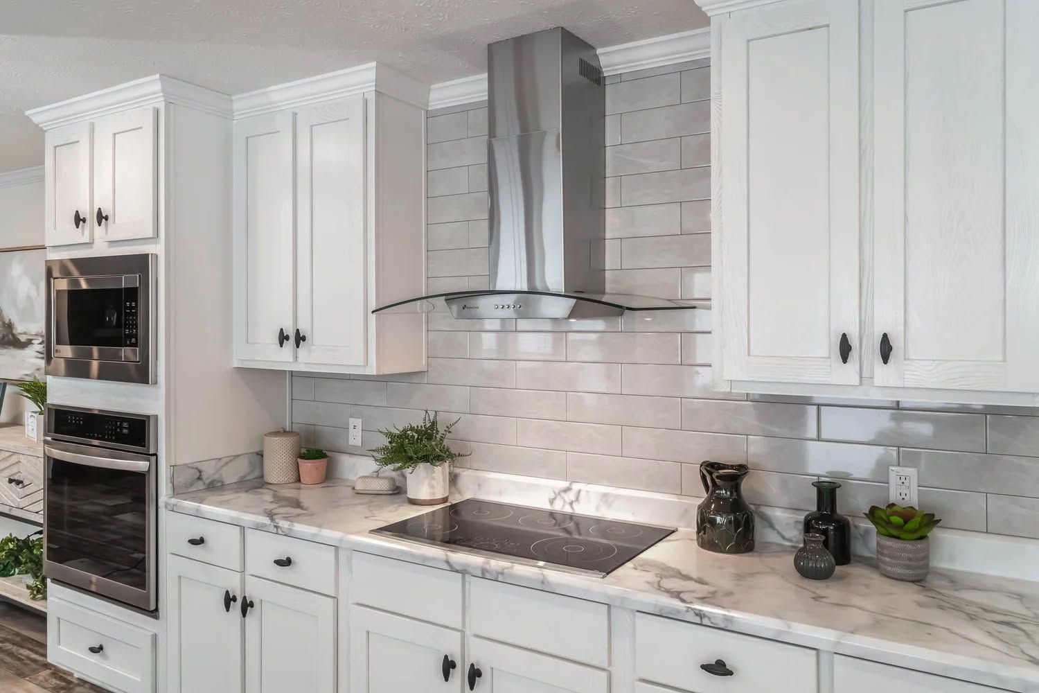 Modern kitchen with white cabinets, marble countertops, and a glass cooktop. Stainless steel range hood and built-in ovens add a sleek touch.