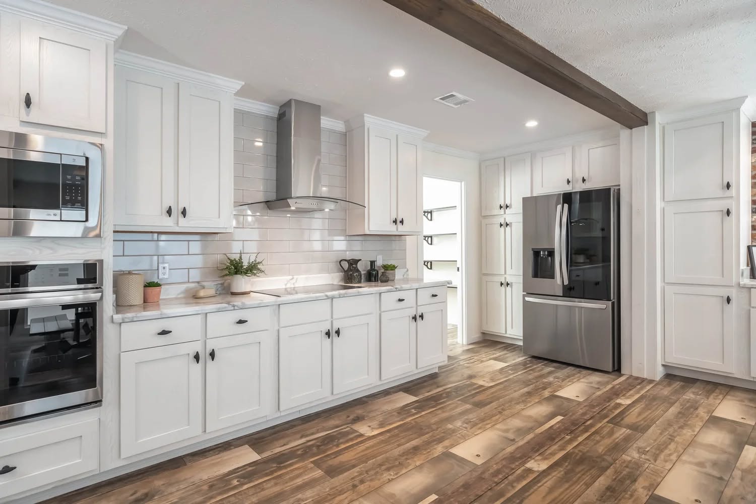 Spacious kitchen with white cabinets, stainless steel appliances, and wooden floors. A beam accents the ceiling, creating a modern, inviting atmosphere.