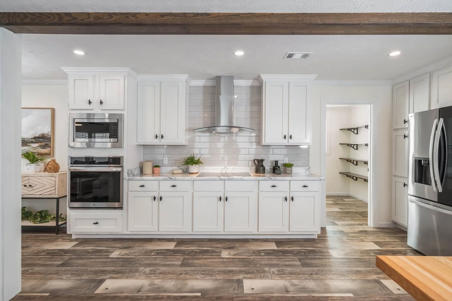 Modern kitchen with white cabinets, stainless steel appliances, and wood floors. A cozy, minimalist space featuring plants and a sleek range hood.