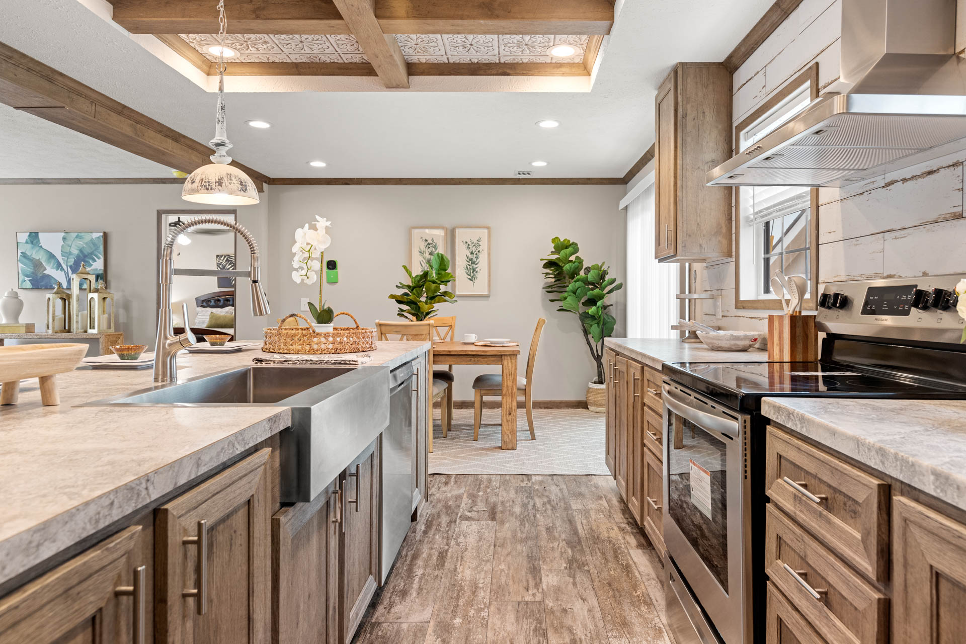Modern rustic kitchen and dining area with wood cabinets and floors, stainless steel appliances, farmhouse sink, pendant lighting, and green plants.