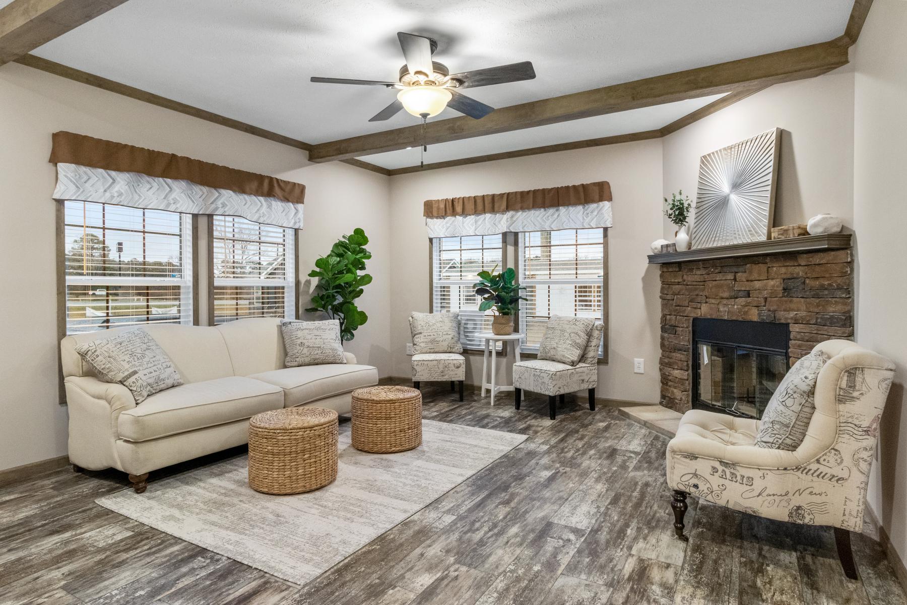 Cozy living room with beige walls and wood accents. Features a cream sofa, patterned chairs, and a stone fireplace. Bright, inviting atmosphere.