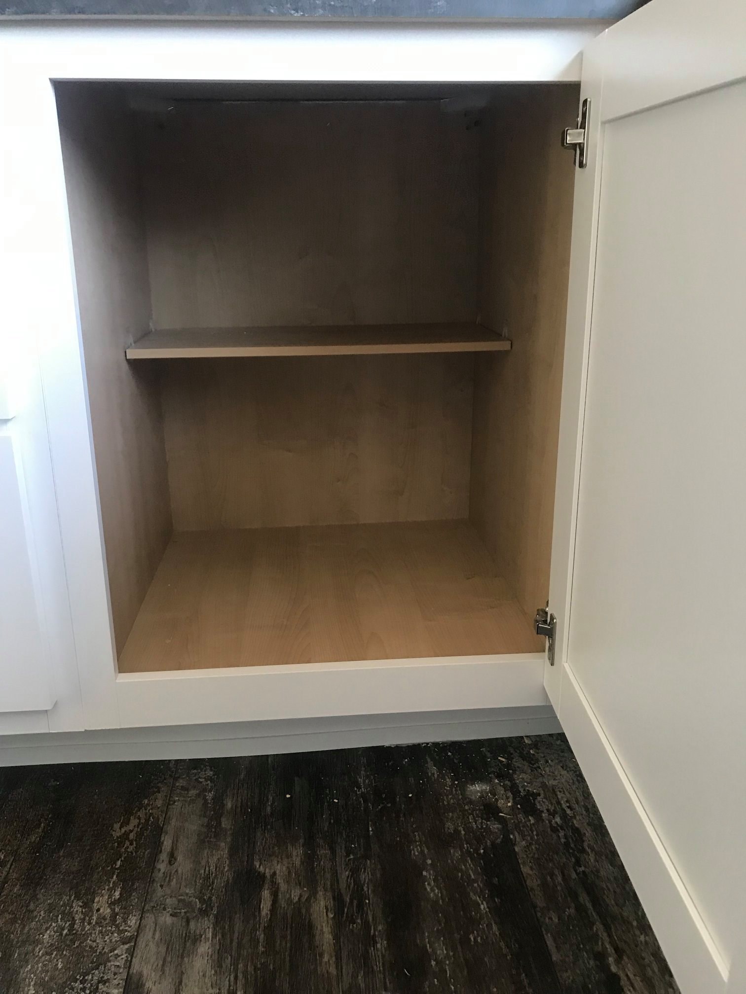 Open white wooden cabinet with a single shelf inside, set against a dark, textured floor. The interior is empty, conveying a minimalist tone.