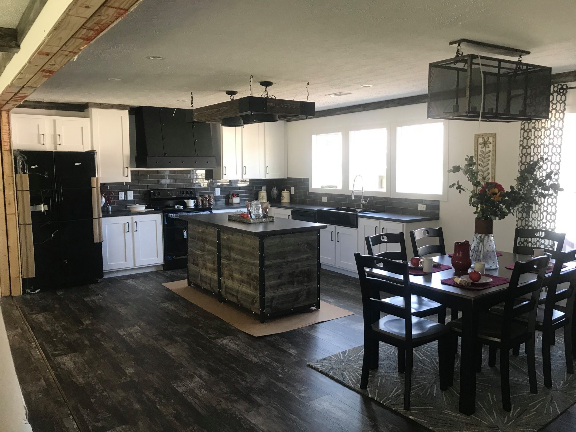 Spacious kitchen with white cabinets, black countertops, and island. Dark wood floors. Dining table with chairs and a vase of flowers. Airy and modern.