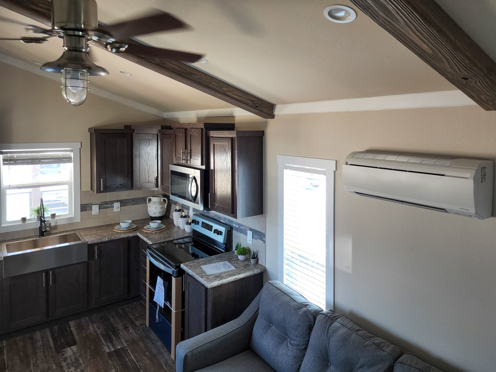Modern kitchen with dark wood cabinets, stainless steel appliances, and a farmhouse sink. A cozy gray sofa and air conditioner are visible. Bright, inviting space.