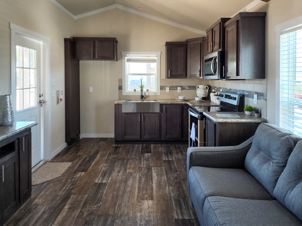 Contemporary kitchen with dark wood cabinets, a window over a farmhouse sink, stainless steel appliances, and light wood flooring. Cozy, inviting atmosphere.