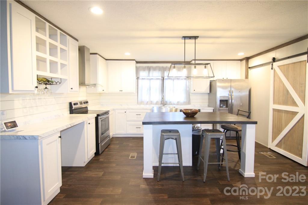 Modern kitchen with white cabinets, dark wood floors, and a central island with bar stools. Stainless steel appliances and a barn door add a rustic touch.