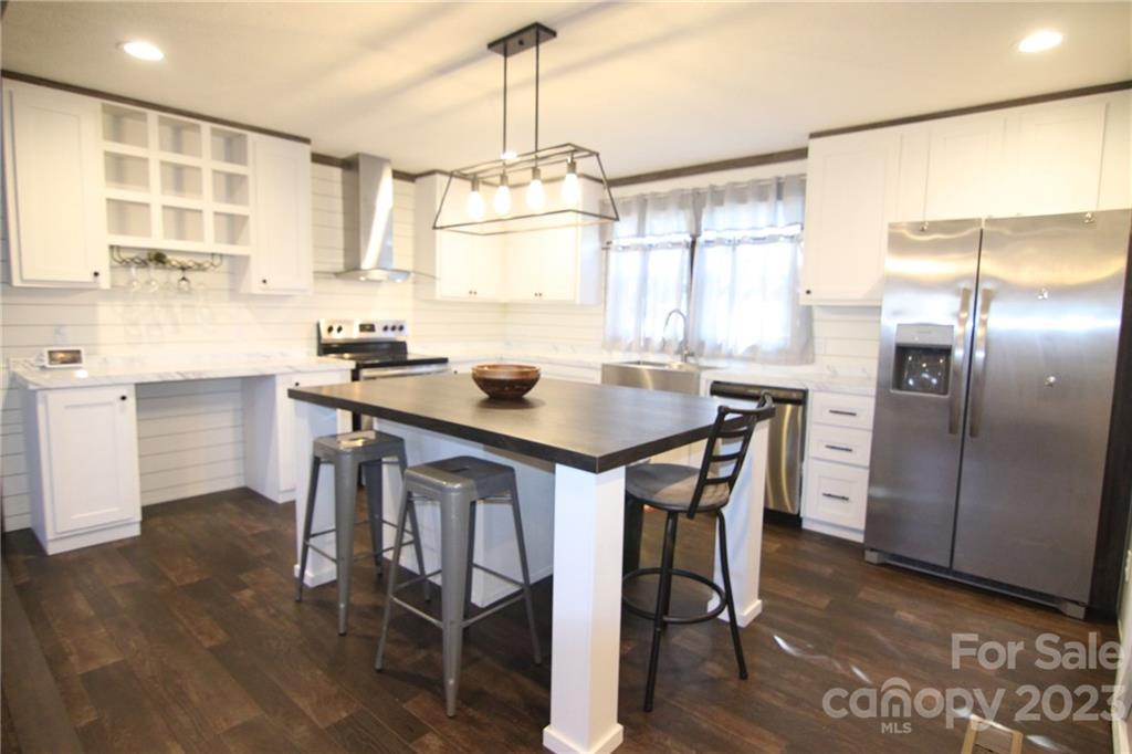 Modern kitchen with white cabinets, stainless steel appliances, dark wood island and floors. Pendant light hangs over the island with stools.