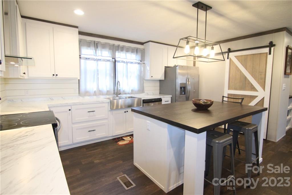 Modern kitchen with white cabinetry, stainless steel appliances, and dark wood flooring. Features an island with stools and a barn door pantry. Warm lighting creates a cozy atmosphere.
