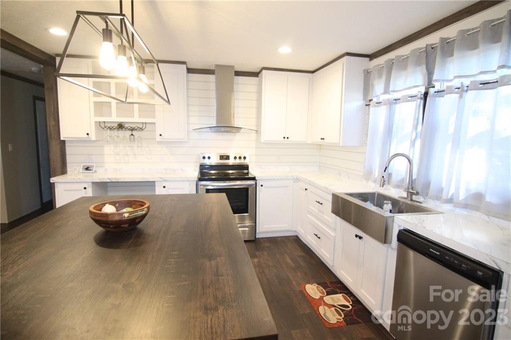 Modern kitchen with white cabinets, dark wood island, and stainless steel appliances. Bright lighting and sheer curtains create a clean, elegant ambiance.