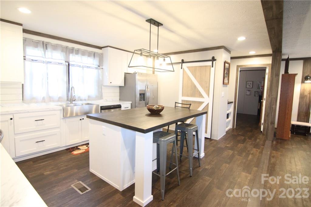 Modern kitchen with a farmhouse vibe, featuring a central island with stools, barn-style sliding door, white cabinets, stainless steel appliances, and warm wood flooring. Bright and inviting atmosphere.