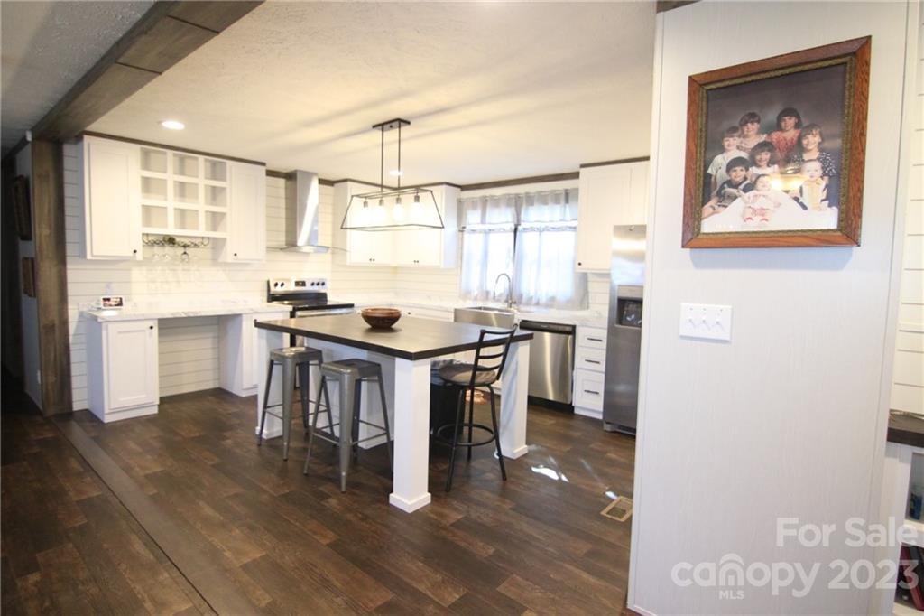 Modern kitchen with white cabinetry, dark wood flooring, and a central island with metal stools. Warm lighting and a family photo create a cozy ambiance.