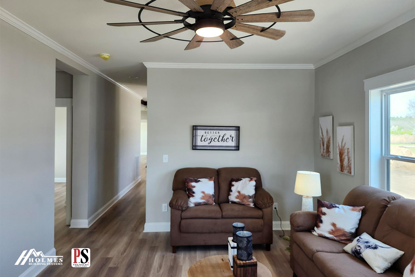 Cozy living room with brown sofas, a cowhide-patterned pillow, and a "Better Together" sign on the wall. A modern ceiling fan and bright window complete the space.