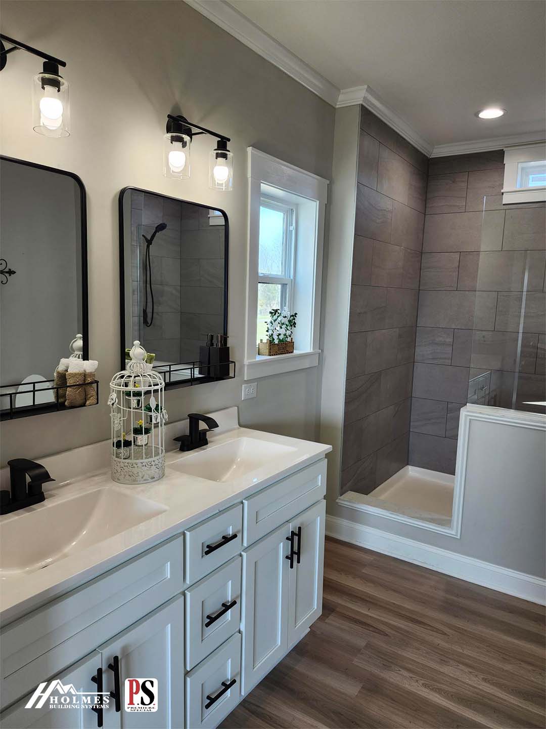 Modern bathroom with dual sinks, white vanity, and black fixtures. Rectangular mirrors with lights above, a window with a small plant, and a walk-in shower with gray tiles. Light wood flooring adds warmth.