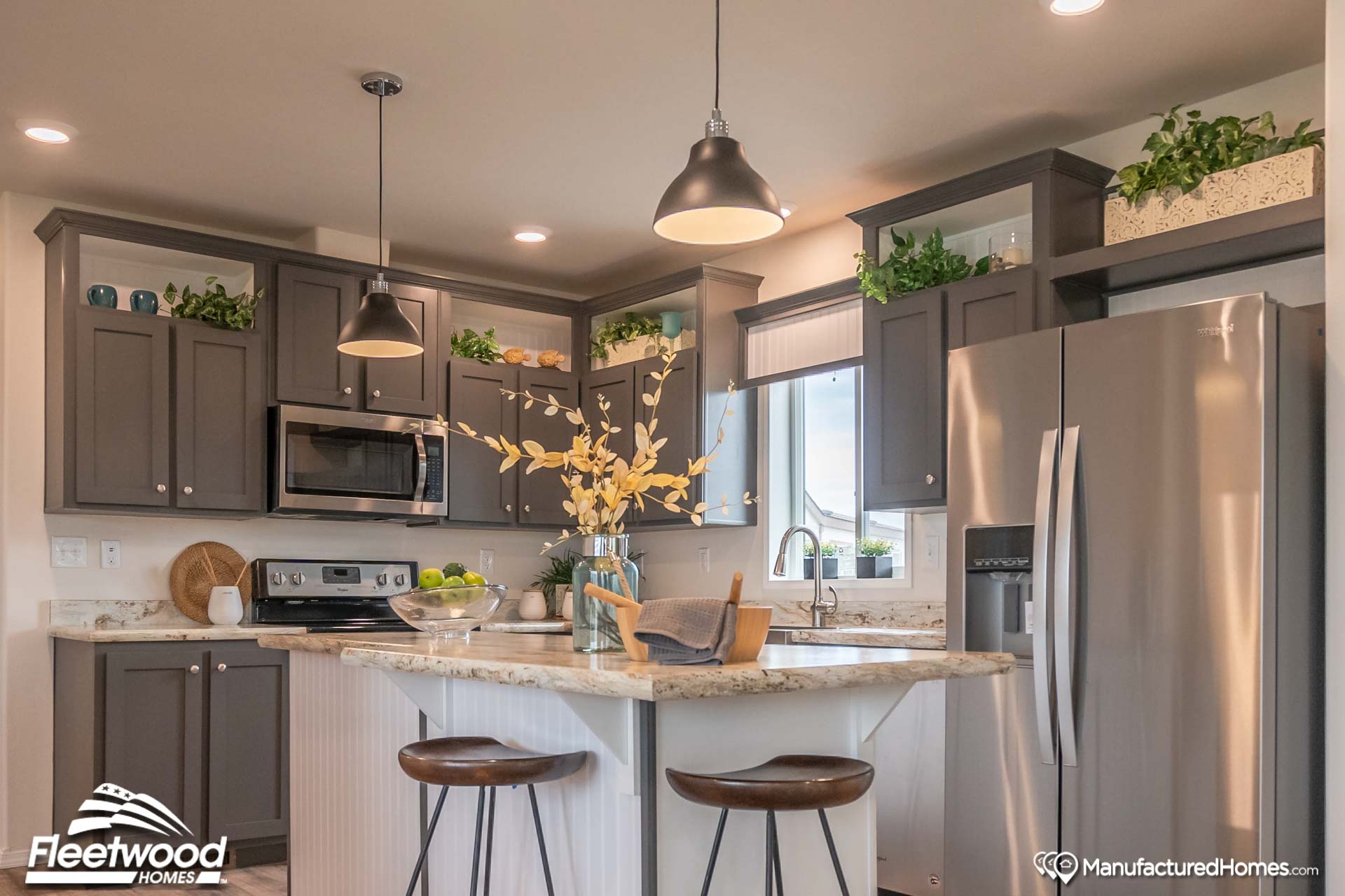 Modern kitchen with dark gray cabinets, stainless steel appliances, and a marble countertop. Two pendant lights hang above a breakfast bar with wooden stools.
