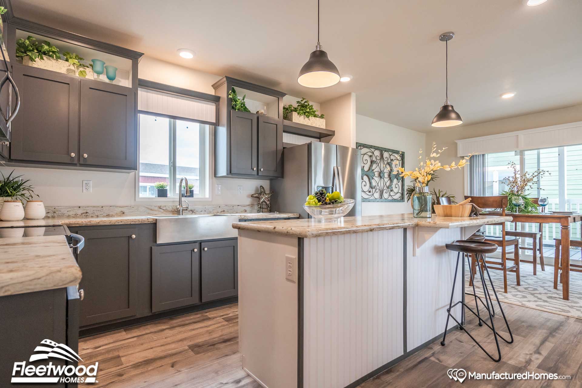 Modern kitchen with dark cabinets, light countertops, and stainless steel appliances. Bar stools at island, dining area in background. Bright, inviting atmosphere.
