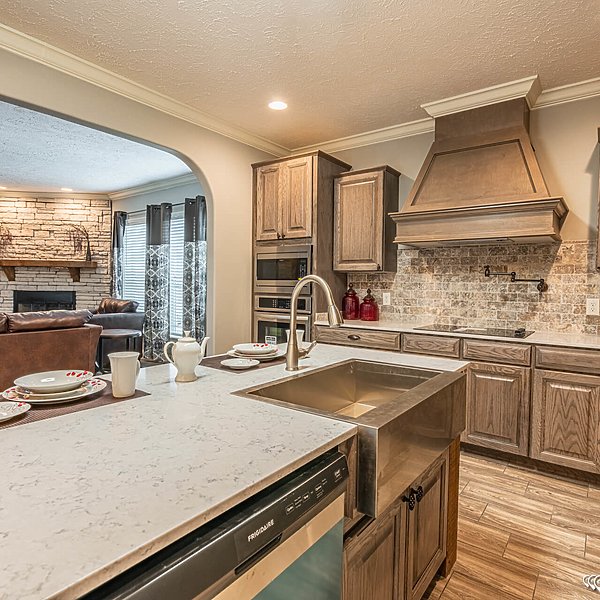 Stylish kitchen with a marble island, stainless steel sink, and wooden cabinetry adjacent to a cozy living area with a stone fireplace and leather sofa.