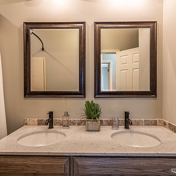 Modern bathroom with dual sinks on a marble countertop, featuring black faucets, decorative plant, and two framed mirrors, creating a clean ambiance.