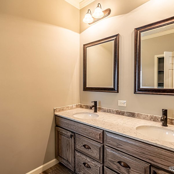 Modern bathroom with dual sinks on a marble countertop, wooden cabinets, and two framed mirrors. Warm lighting creates a cozy, elegant ambiance.
