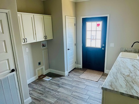 A laundry room with light wood flooring, white cabinets, and beige walls. A dark blue door leads outside, complementing the calm, neutral tones.