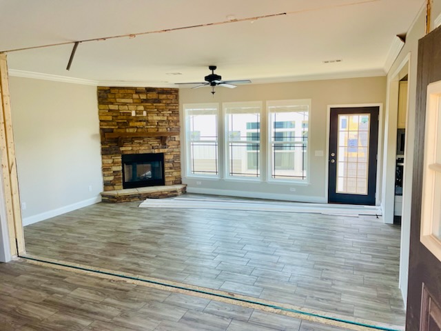 Spacious living room with wooden floor, stone fireplace, and ceiling fan. Large windows and a glass door let in ample light, creating a welcoming ambiance.