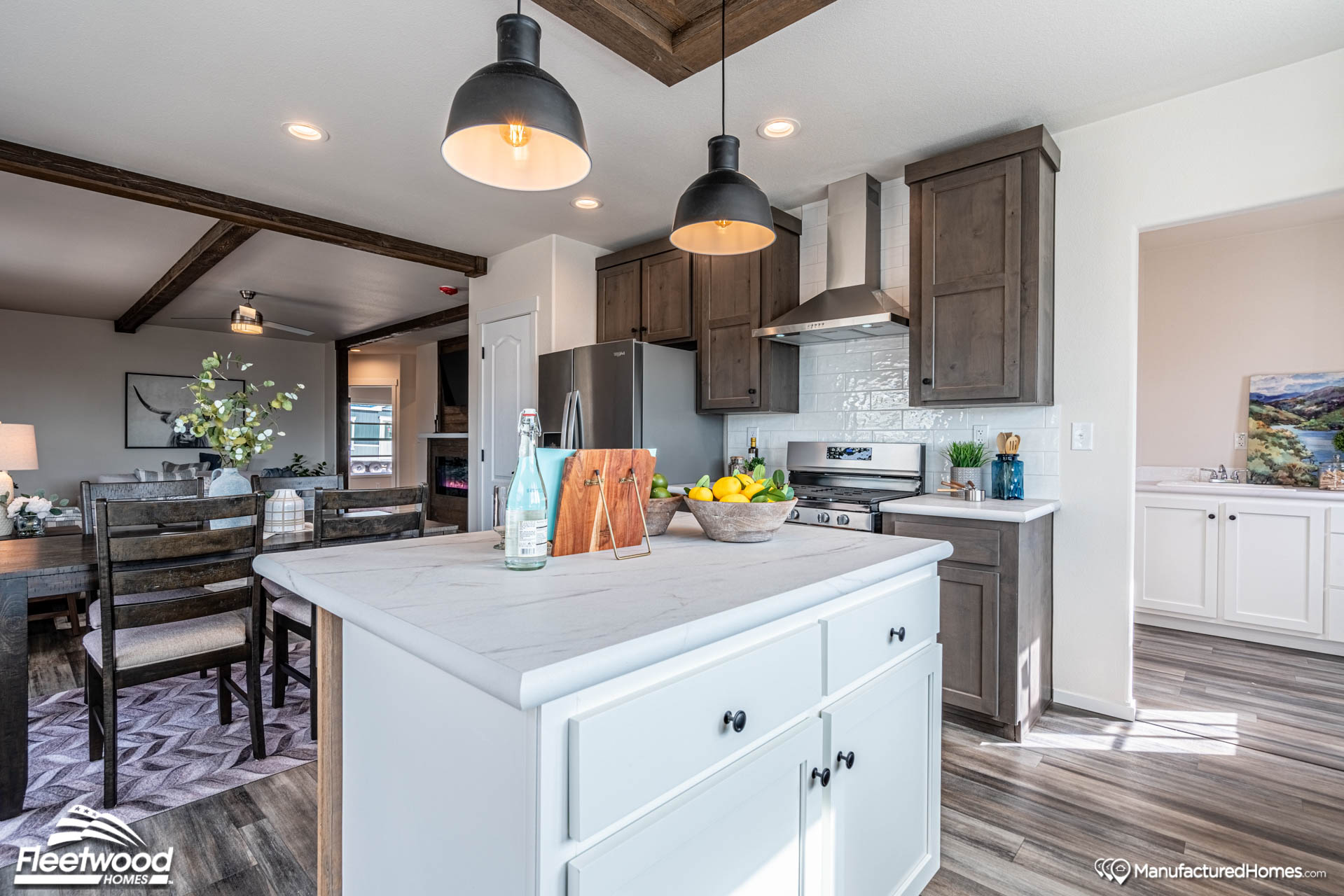 Modern kitchen with white island, dark cabinets, stainless steel appliances, and pendant lights. Dining area in the background, bright and inviting.
