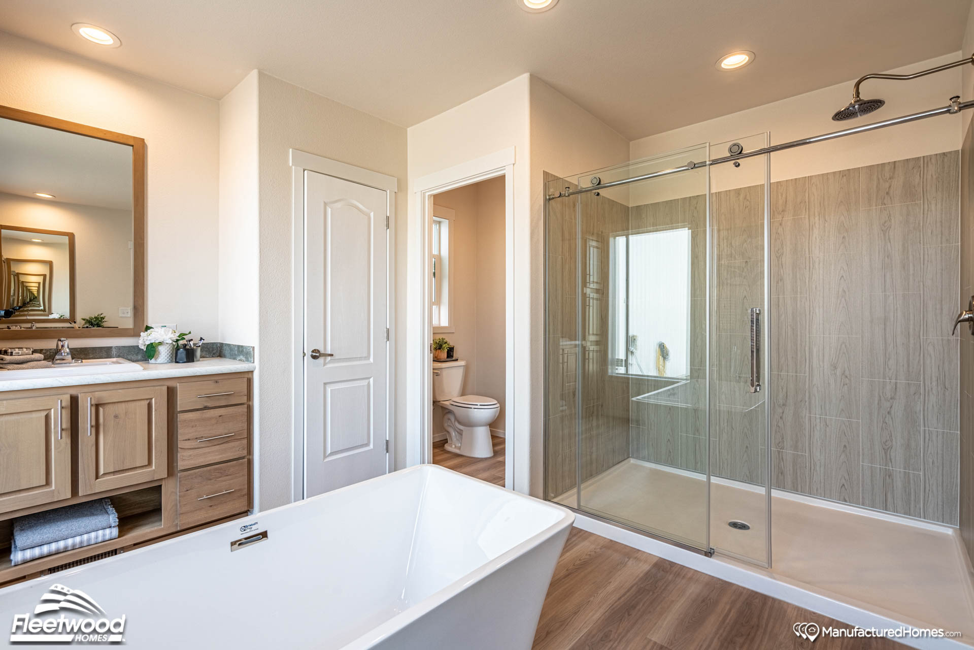 Modern bathroom with a freestanding tub, glass-enclosed shower, and vanity with wood cabinets. Neutral tones; bright, spacious, and elegant atmosphere.