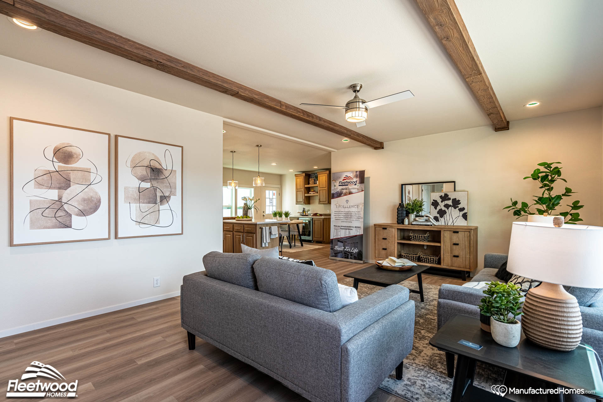 Modern living room with gray sofas, wooden beams, abstract art, and potted plants. Open layout revealing kitchen and dining area. Warm and inviting ambiance.