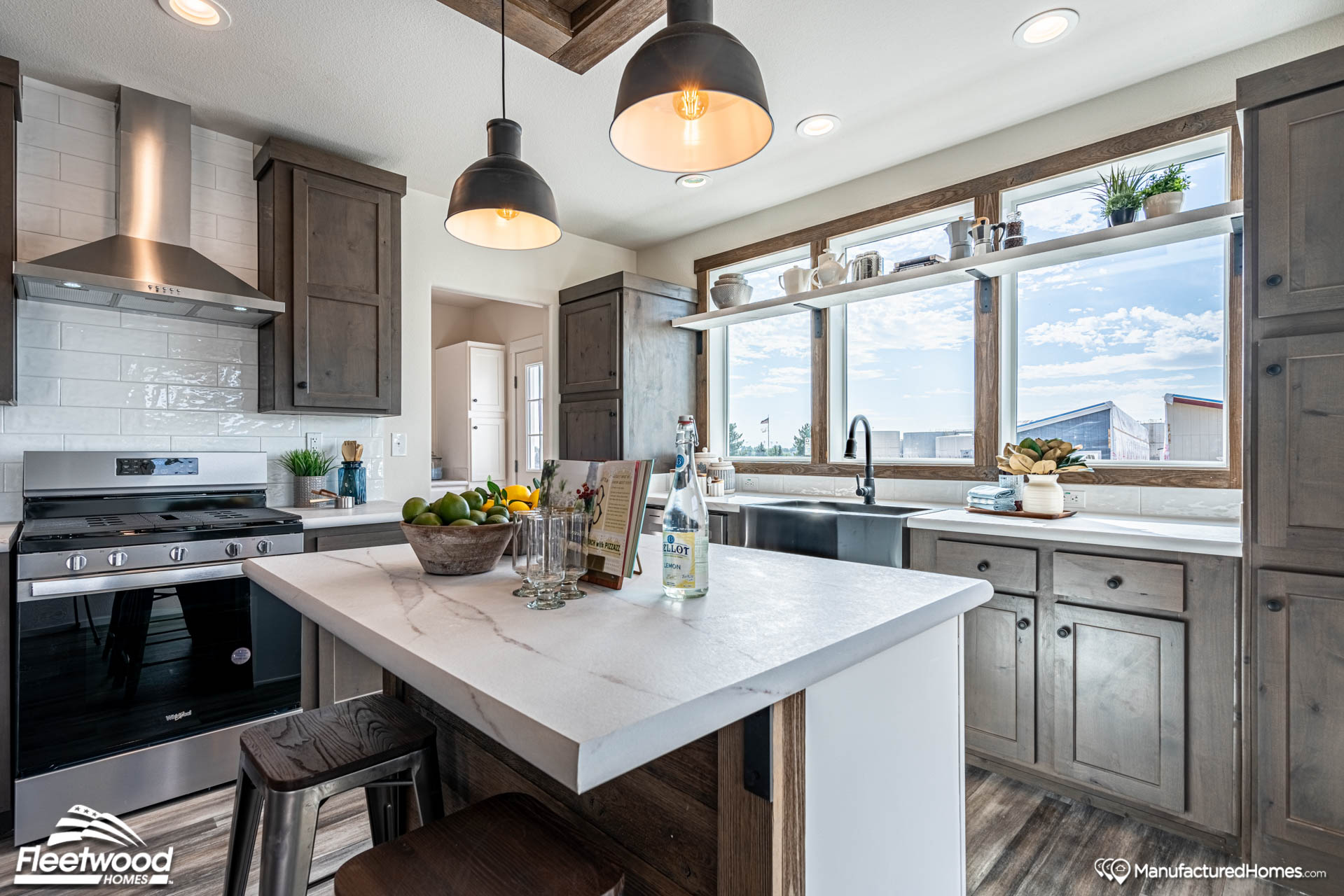 Modern kitchen with rustic cabinets, marble island, and stainless steel appliances. Large windows offer natural light and outdoor view. Cozy and inviting.