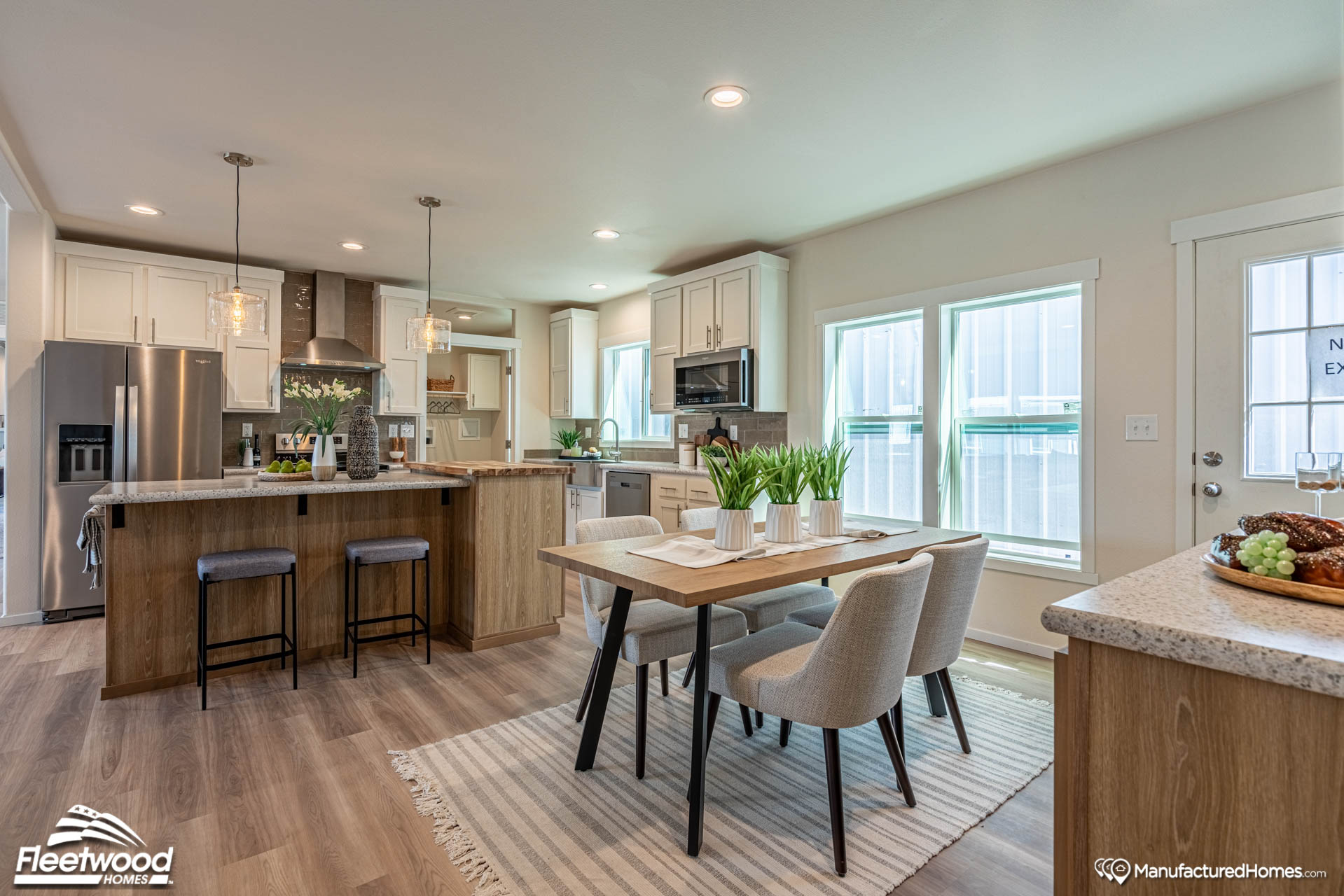 Modern kitchen and dining area with natural light. Features wood floors, a central island with barstools, a wooden dining table, and chic decor.